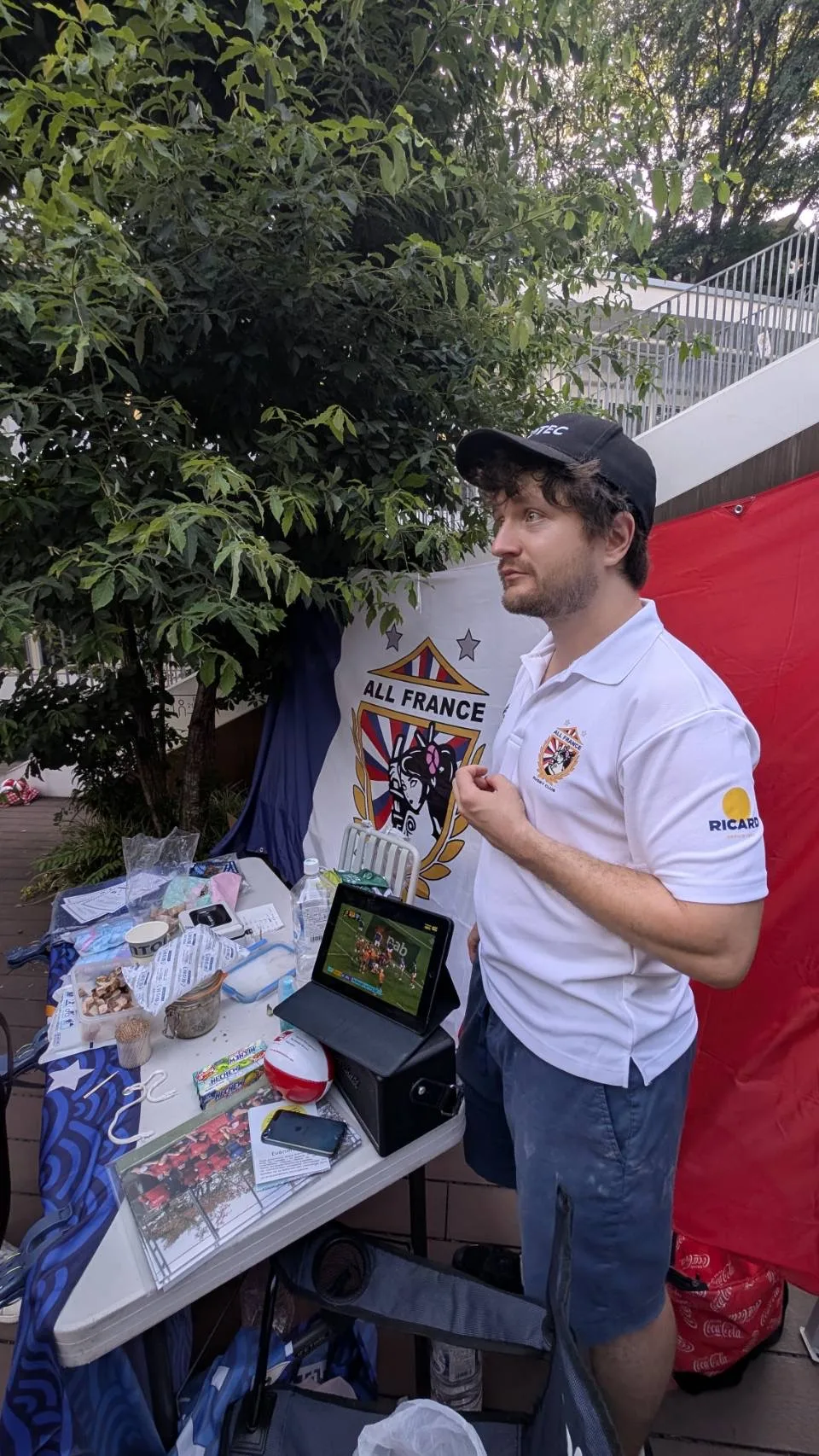 Un membre de l’AFRC devant la table et la bannière du club pendant les célébrations du 14 Juillet à Tokyo.