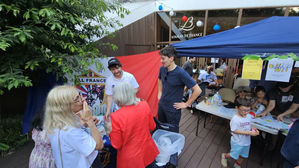 Visitors and AFRC members gather around the All France Rugby Club stand during the French Embassy’s Bastille Day celebration in Tokyo.
