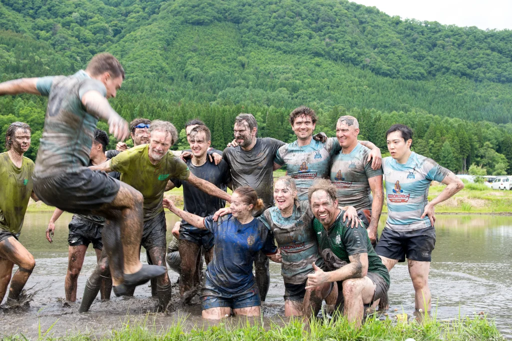 Mud-covered All France Rugby Club players pose together in a rice field after playing Tambo Rugby in Hakuba.