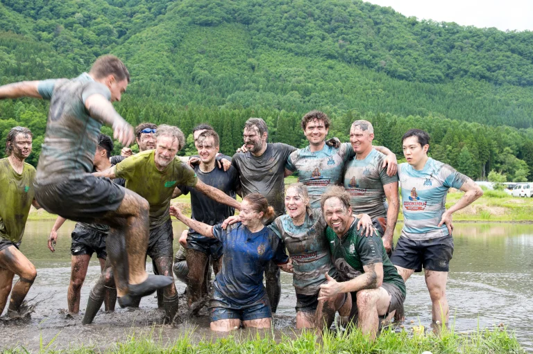 Mud-covered All France Rugby Club players pose together in a rice field after playing Tambo Rugby in Hakuba.