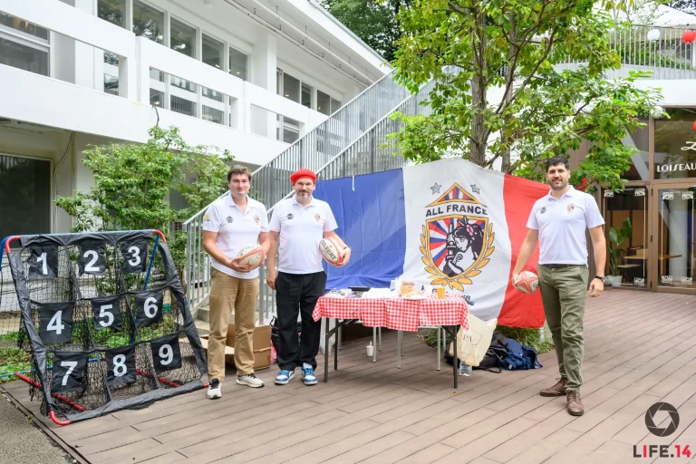 Three All France Rugby Club members stand beside the AFRC flag and rugby passing target at Vive l’Art de Vivre in Tokyo.